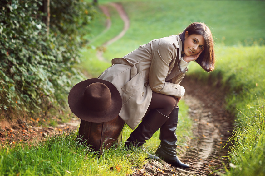 Beautiful woman seated on a vintage leather suitcase .